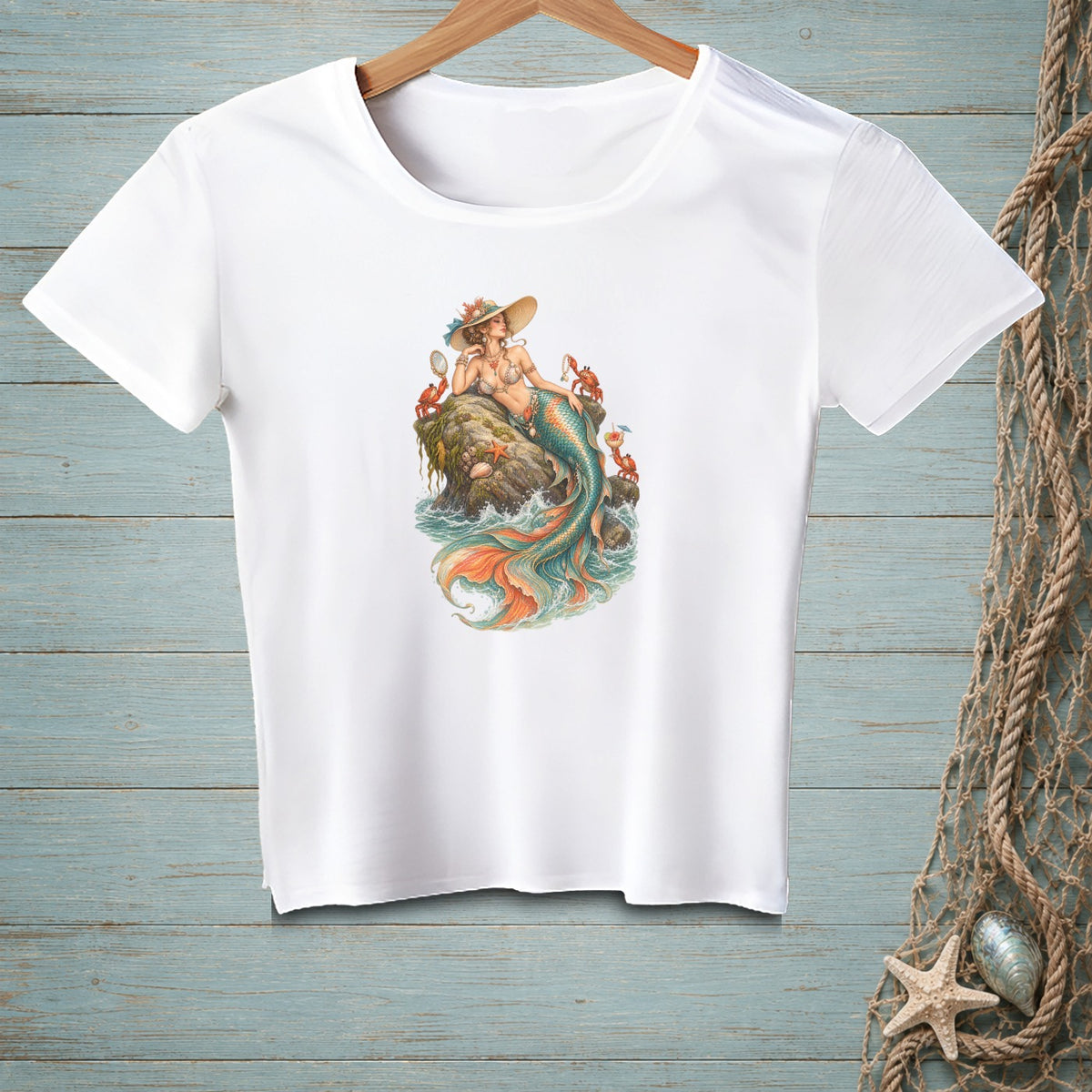 White t-shirt with a mermaid, crabs, and starfish illustration on a rock in the sea.