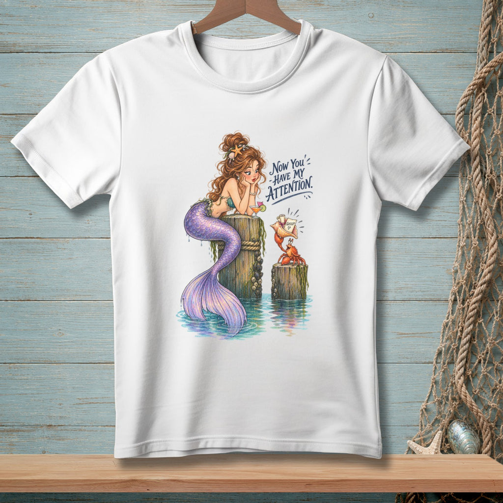 White t-shirt with illustration of a mermaid and crab, text reads "Now You' have my attention."