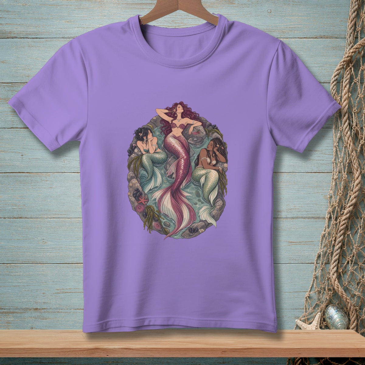 Three mermaids with colorful tails lounge within an oval frame of seaweed and shells.