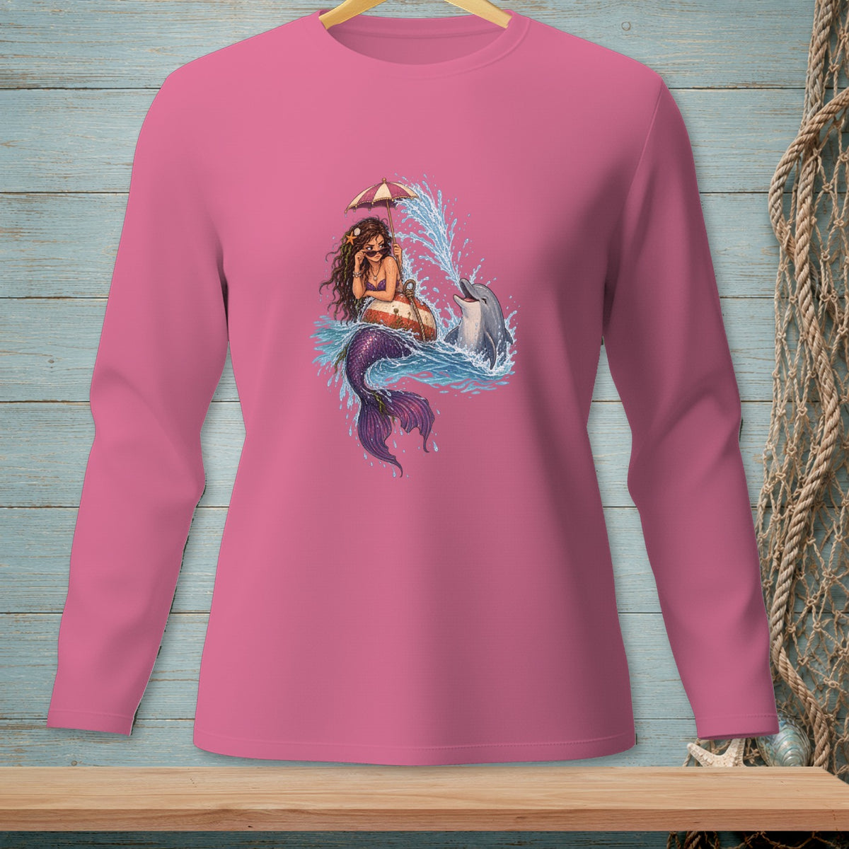 Mermaid with umbrella and dolphin jumping in ocean waves graphic on pink long-sleeve shirt.