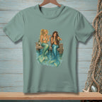 Two mermaids with wine glasses sitting on a dock with blue water.
