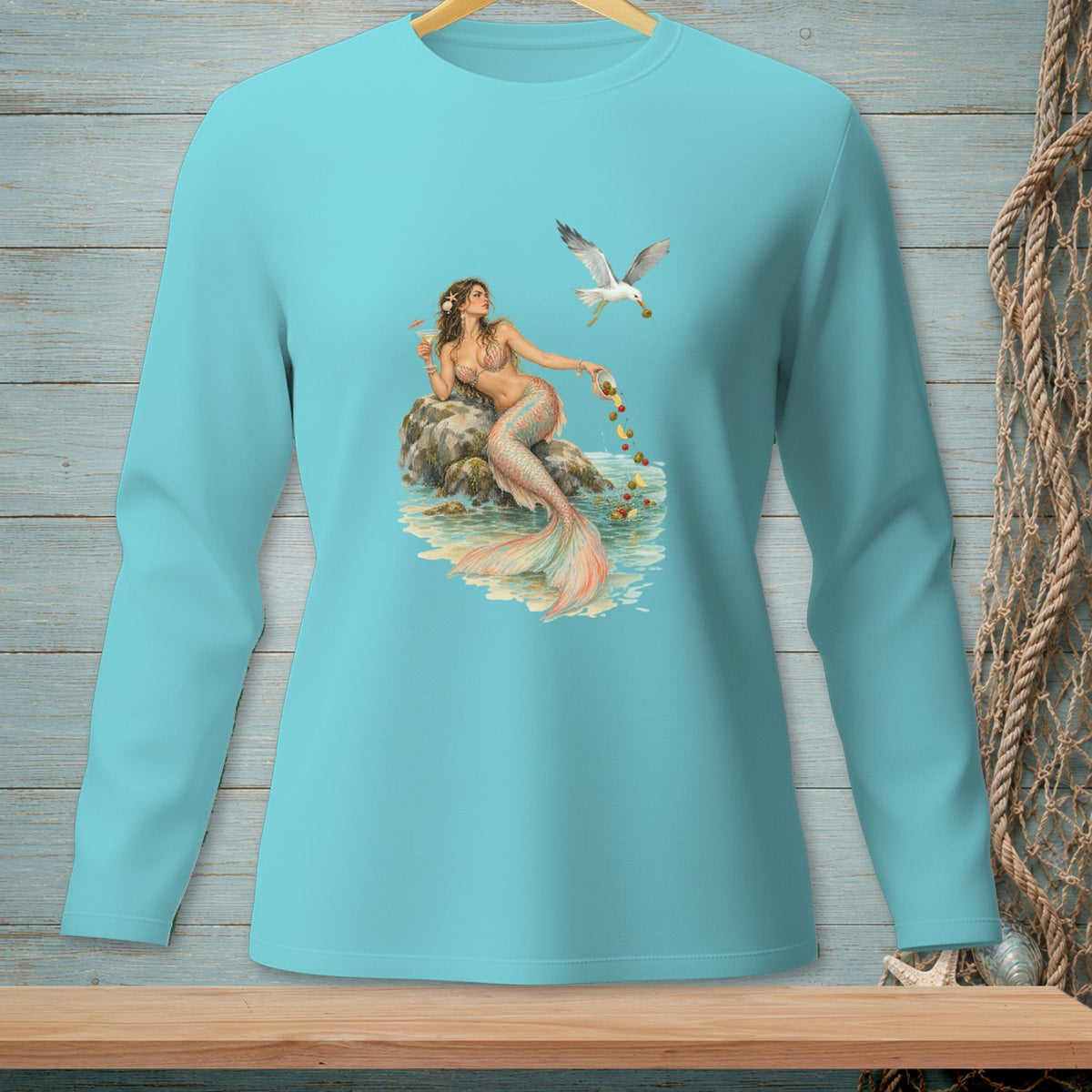 Teal long-sleeve shirt featuring a mermaid sitting on rocks, feeding a seagull.