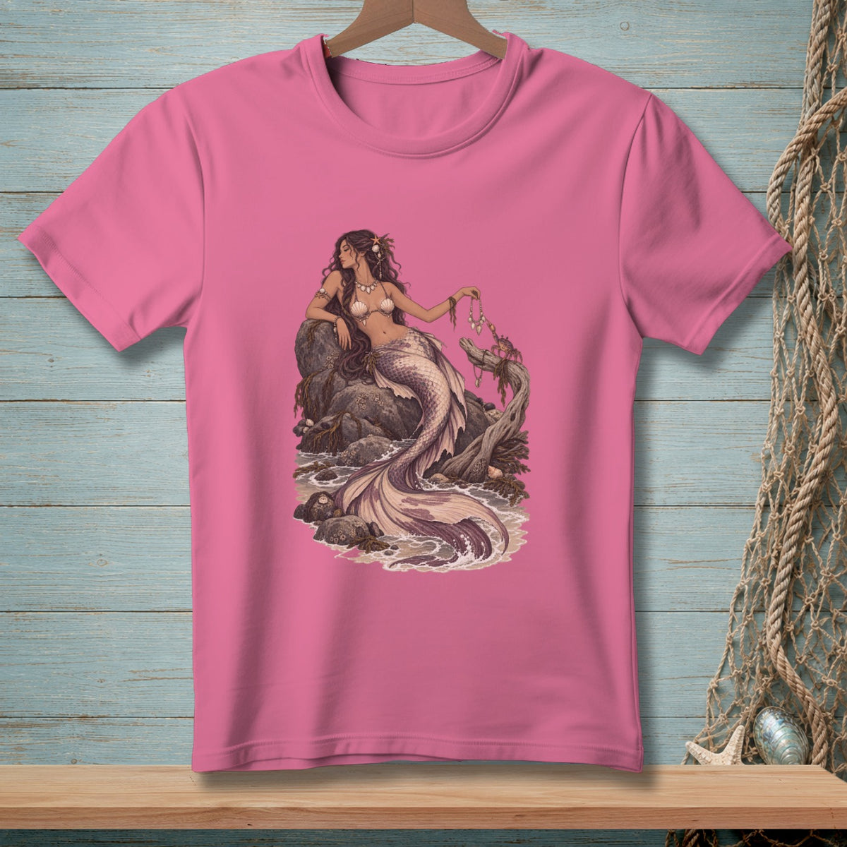 Pink t-shirt with a detailed illustration of a mermaid sitting on rocks by the sea.