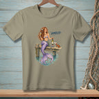 Mermaid with wine and books on dock, text "HANDLED", crab, and starfish decor.