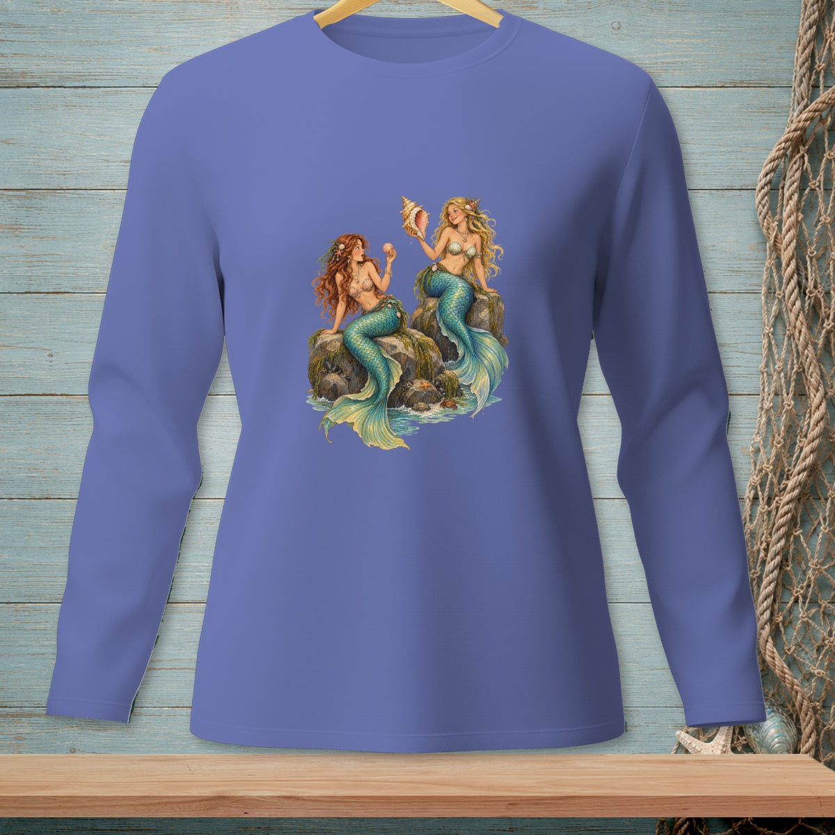 Long sleeve shirt with two mermaids sitting on rocks holding a seashell.