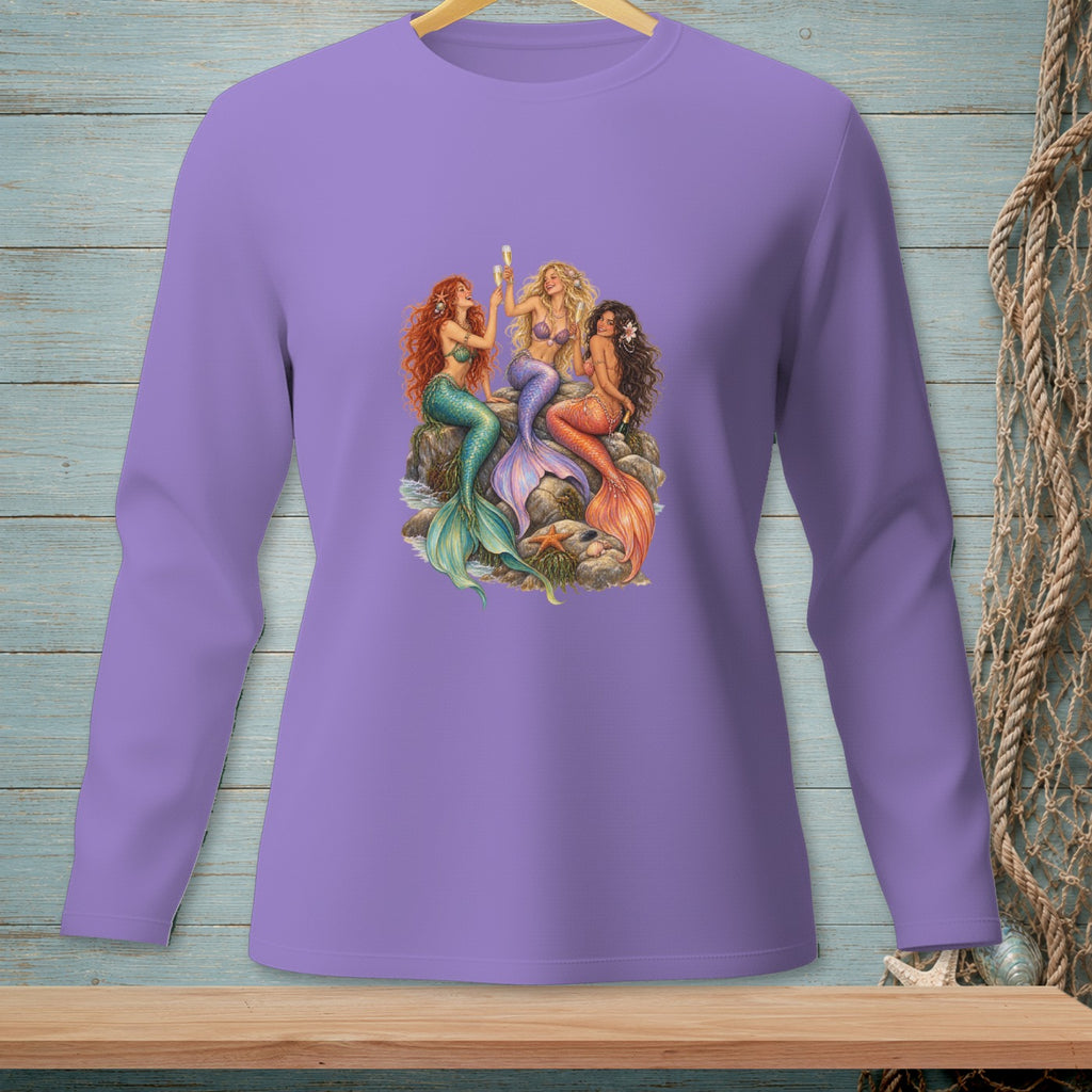Three mermaids with colorful tails sit on rocks, raising champagne glasses.