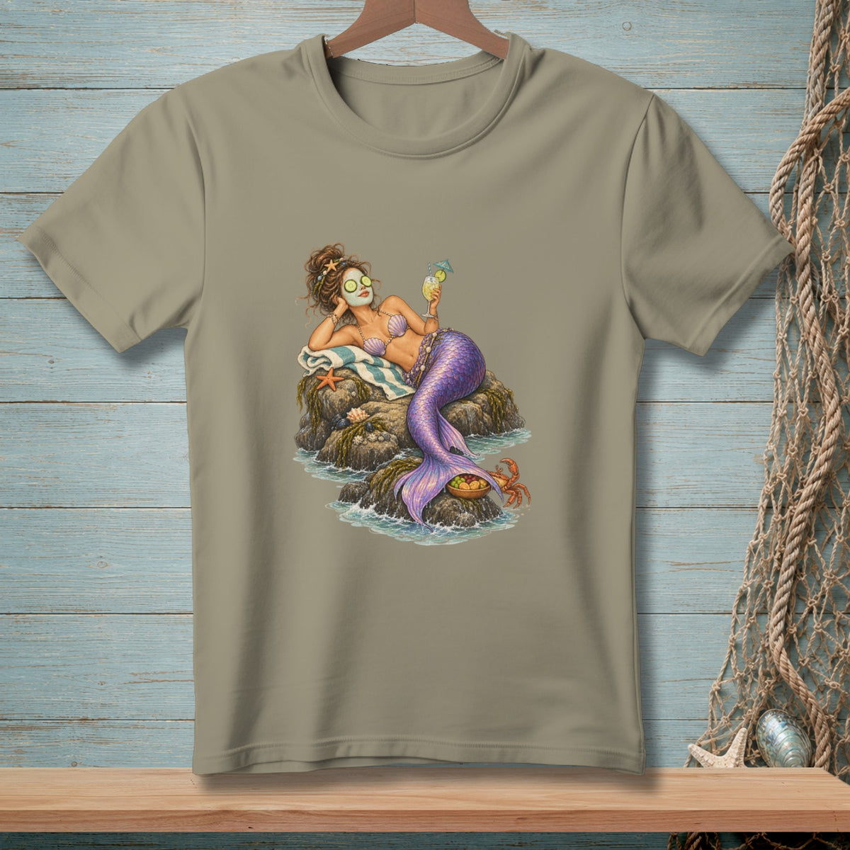 Mermaid relaxing on rocks with a drink and a crab, printed on a tan t-shirt.