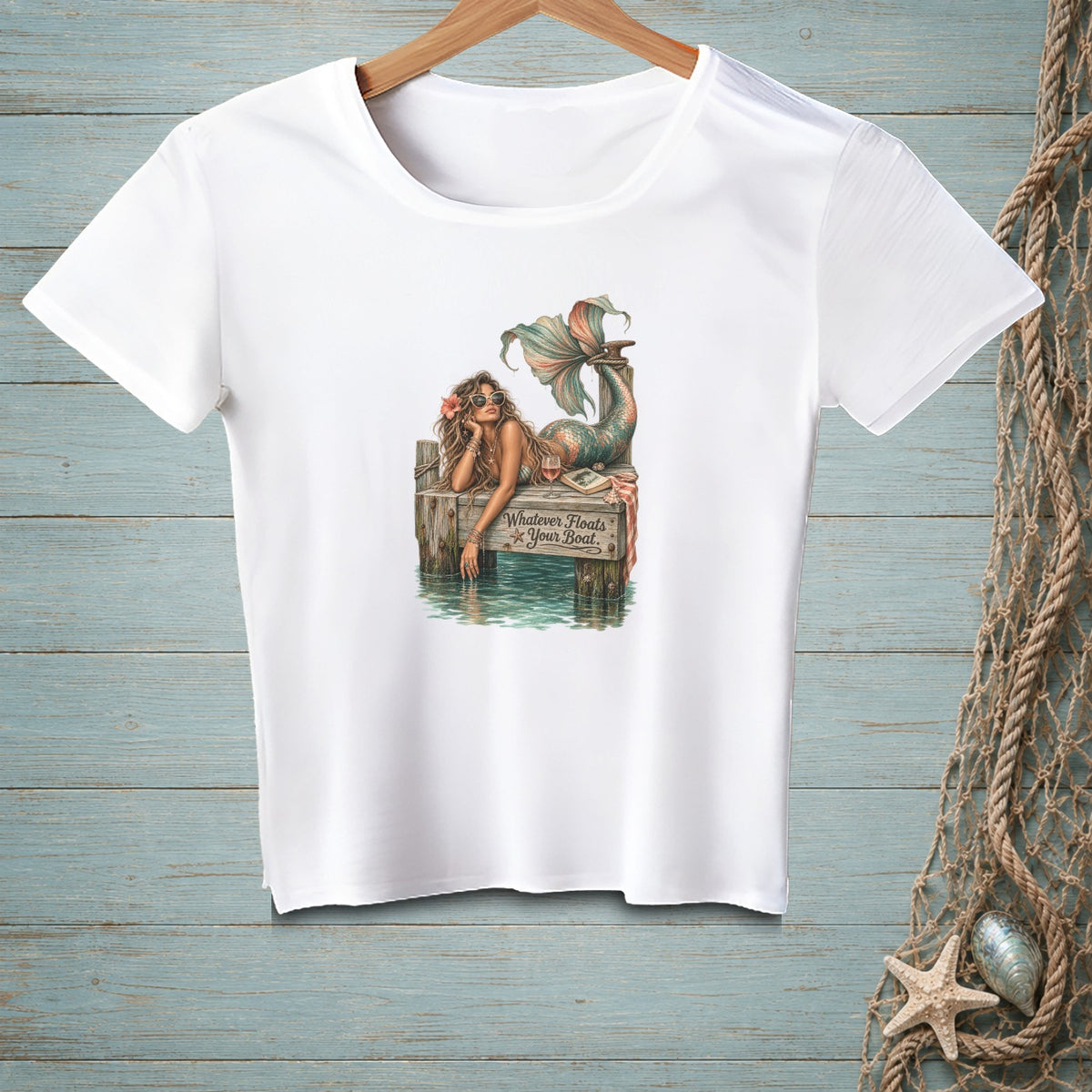 White t-shirt graphic of a mermaid on a dock with text "Whatever Floats Your Boat."
