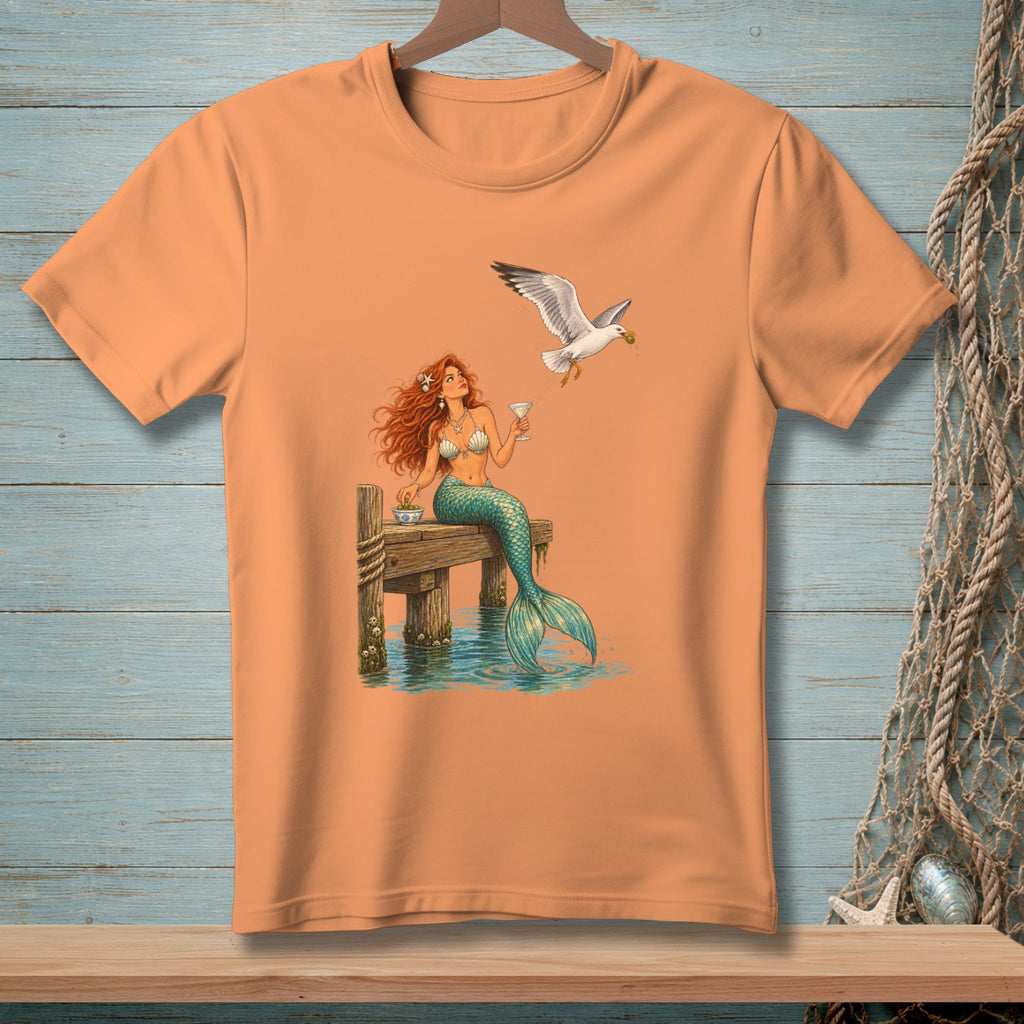 Mermaid with red hair and tail sits on a dock with a seagull flying by.