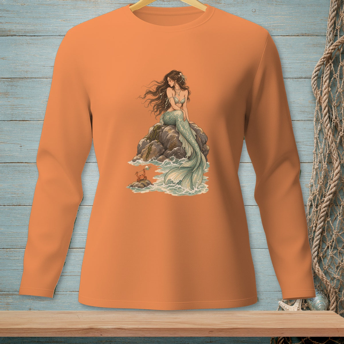 Long sleeve orange shirt with a mermaid sitting on rocks by the sea.