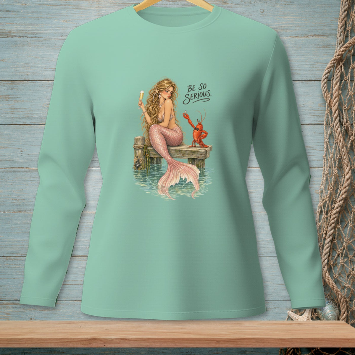 Mermaid with lobster on dock, holding champagne, with text "BE SO SERIOUS."