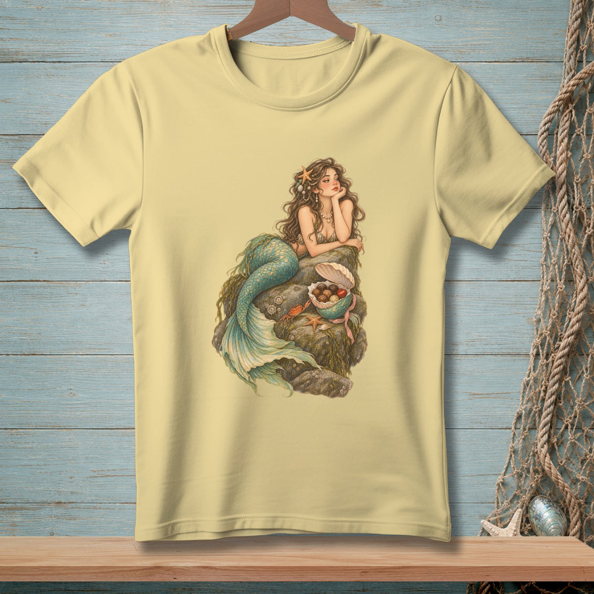 Yellow t-shirt with a mermaid lounging on rocks, holding shells and sea treasures.