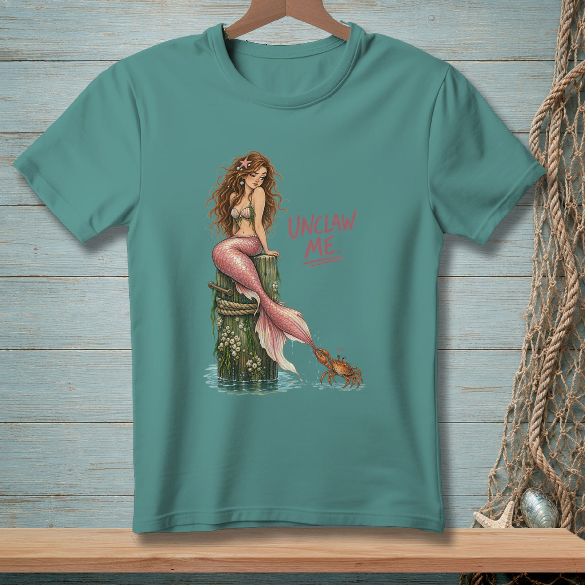 Teal t-shirt featuring a mermaid sitting on a piling with a crab.