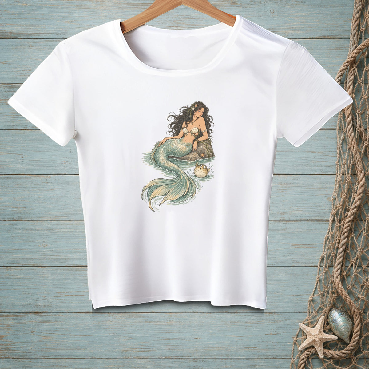 White t-shirt with a drawing of a mermaid and a pufferfish on a rock.