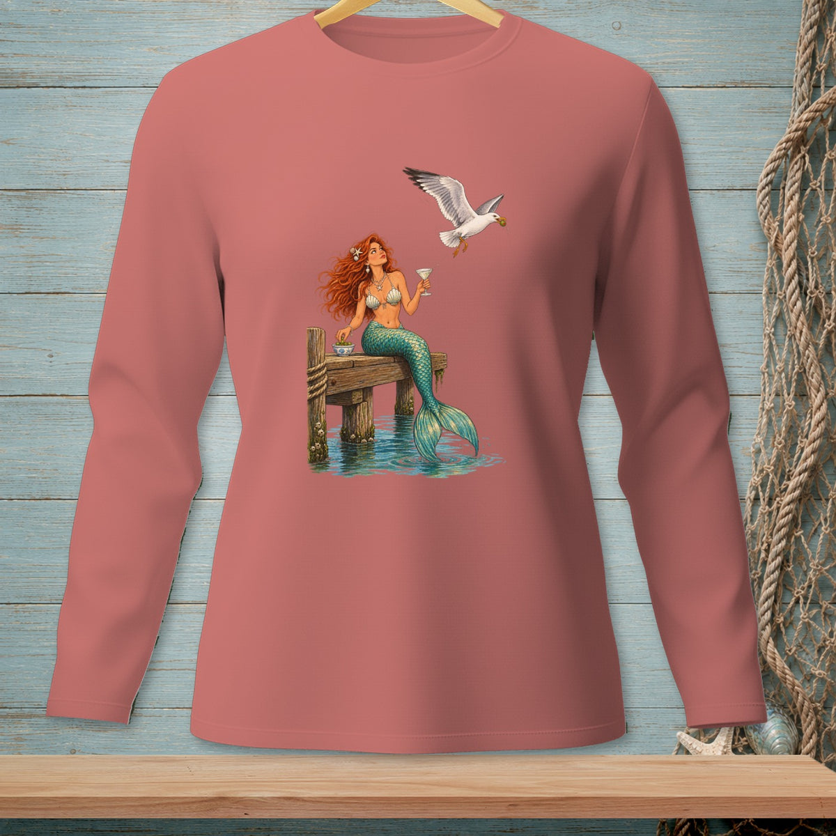 Mermaid sitting on dock with drink and a seagull flying nearby.