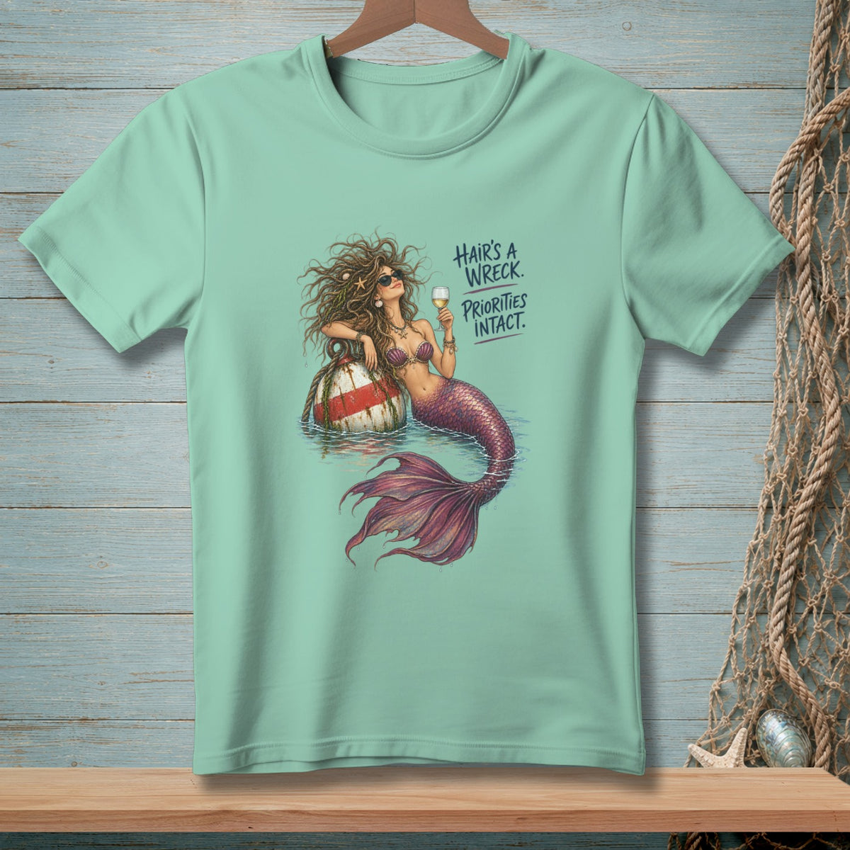 Light mint t-shirt with a mermaid illustration and text that reads "Hair's a wreck. Priorities intact."