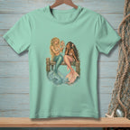 Two mermaids sitting on a pier, one holding a mirror, on a mint t-shirt.