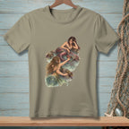 Two mermaids on rocks by the water with a painted illustration on a tan t-shirt.