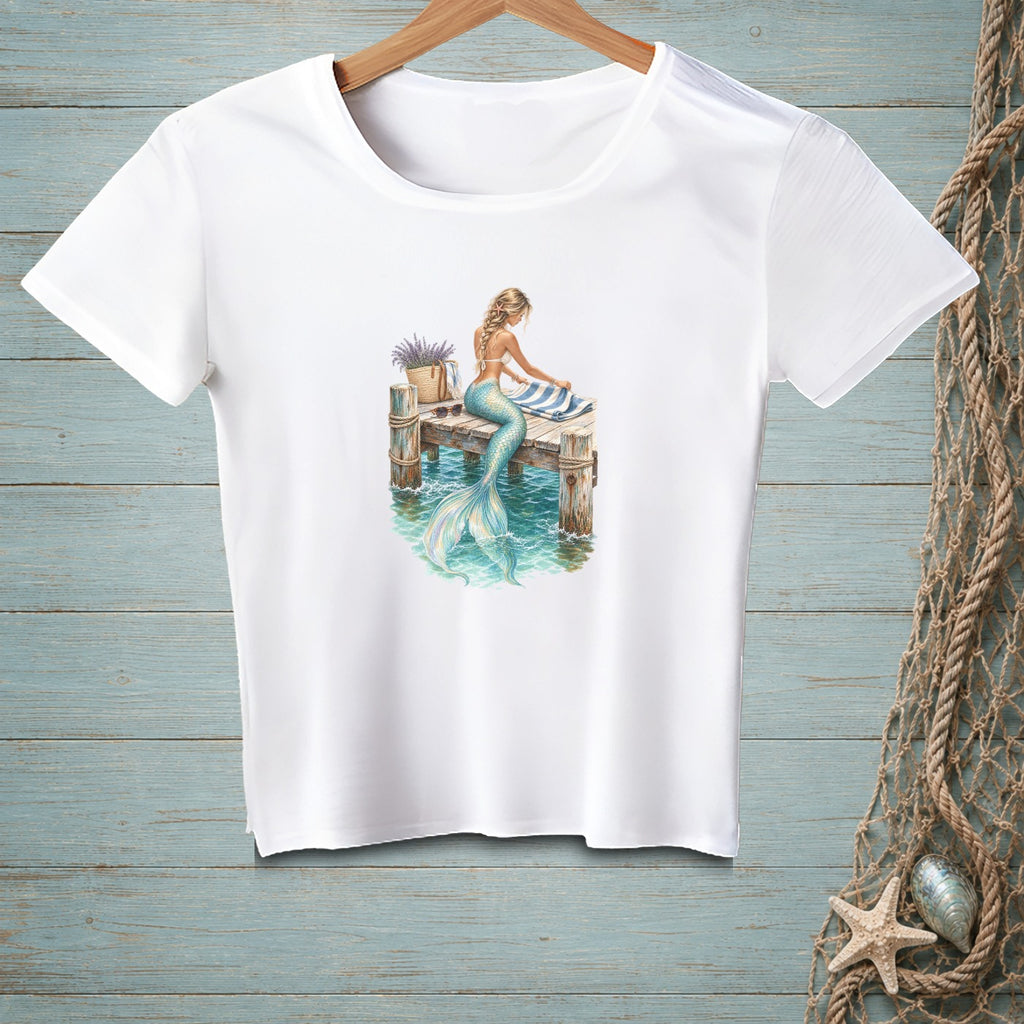 White t-shirt with a mermaid sitting on a dock, her tail in the water.