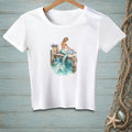 White t-shirt with a mermaid sitting on a dock, her tail in the water.