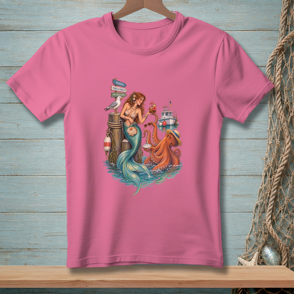 Mermaid and octopus on a dock with signpost, boat, and seagull graphic on pink t-shirt.