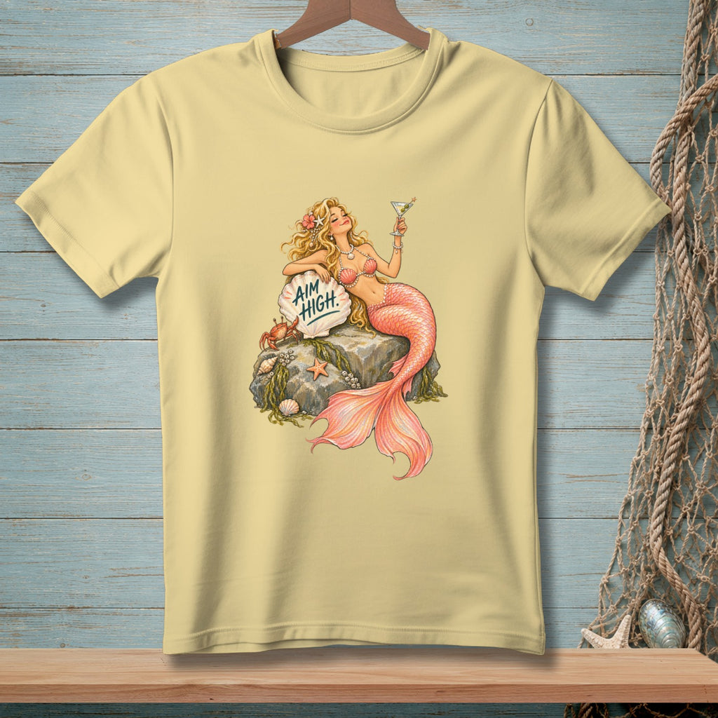 Pale yellow t-shirt with a blonde mermaid holding a cocktail, sitting on a rock with text.