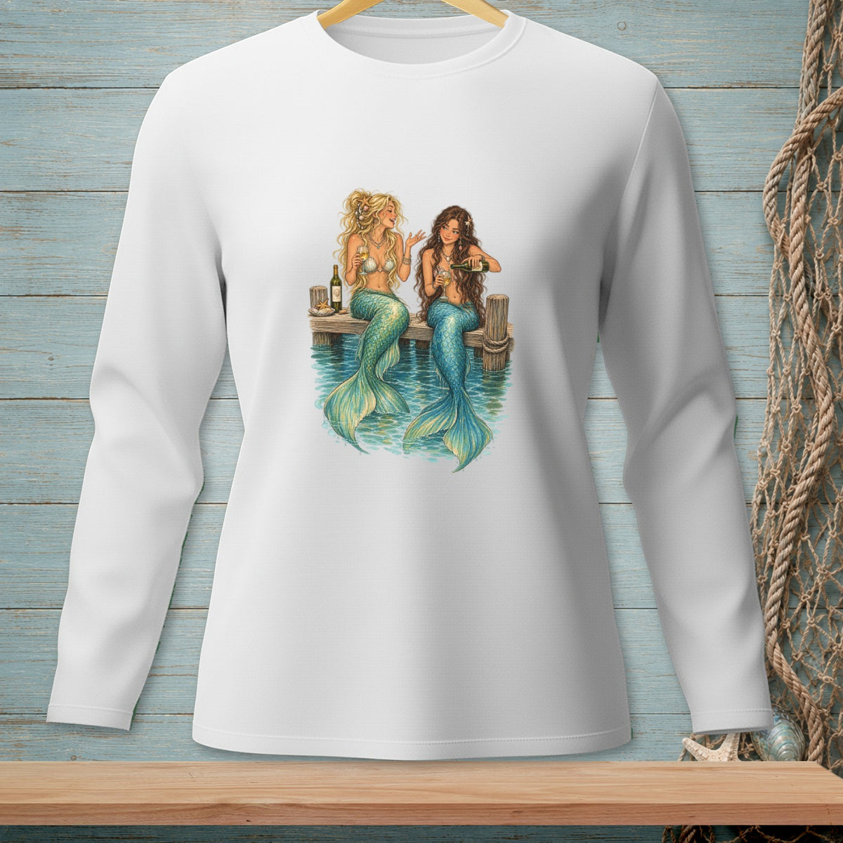 Two mermaids with blue tails sit on a dock, drinking from glasses.