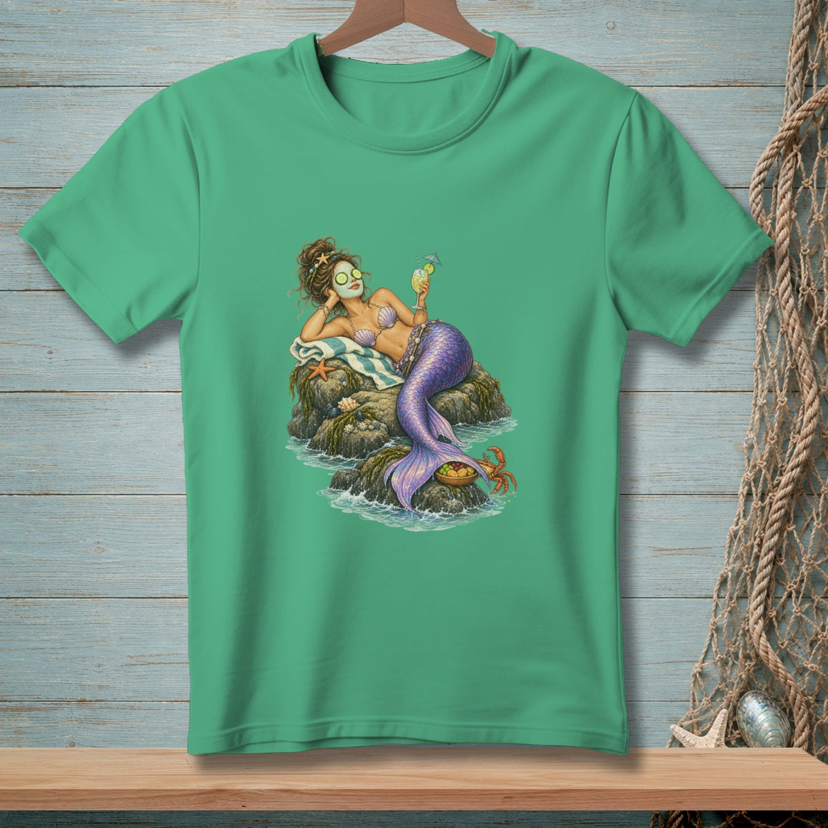 Green t-shirt with a mermaid relaxing on rocks, holding a drink.