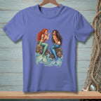 Two mermaids sit on rocks in the ocean, one with red hair, one with dark hair.
