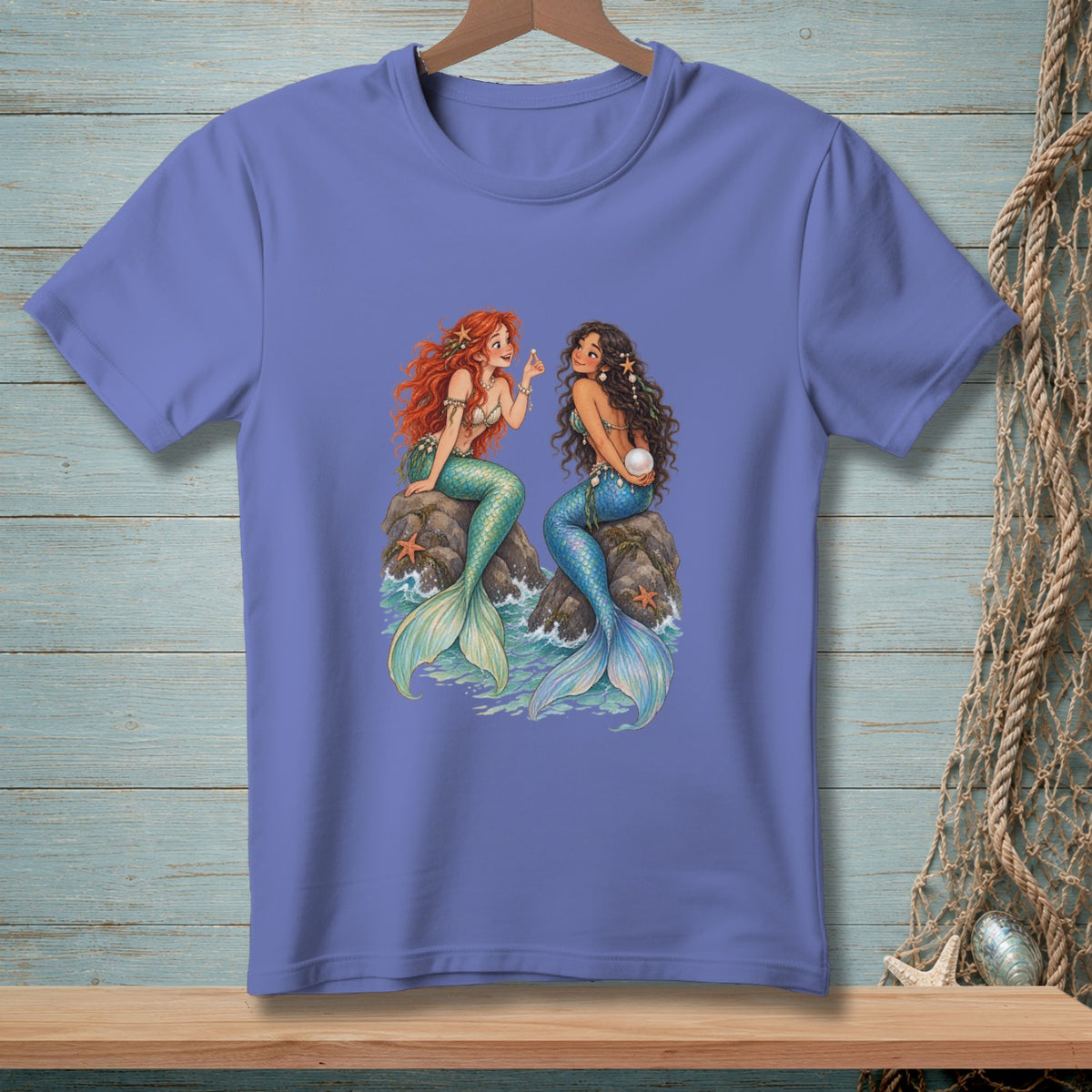 Two mermaids sit on rocks in the ocean, one with red hair, one with dark hair.