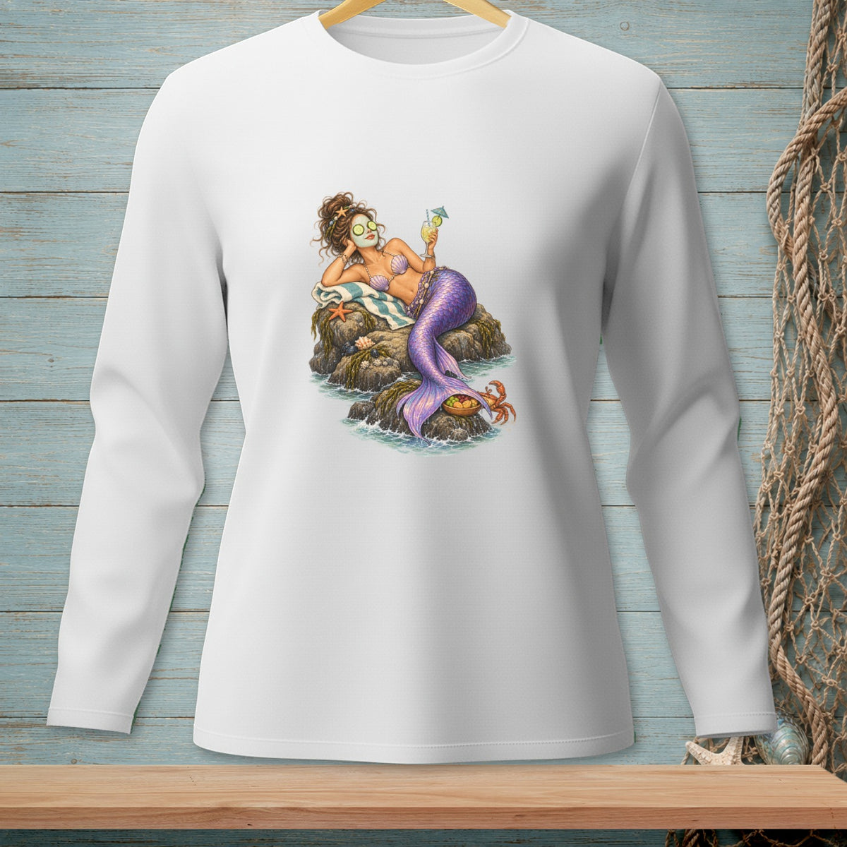 White long-sleeve shirt with a mermaid relaxing on rocks, holding a drink.
