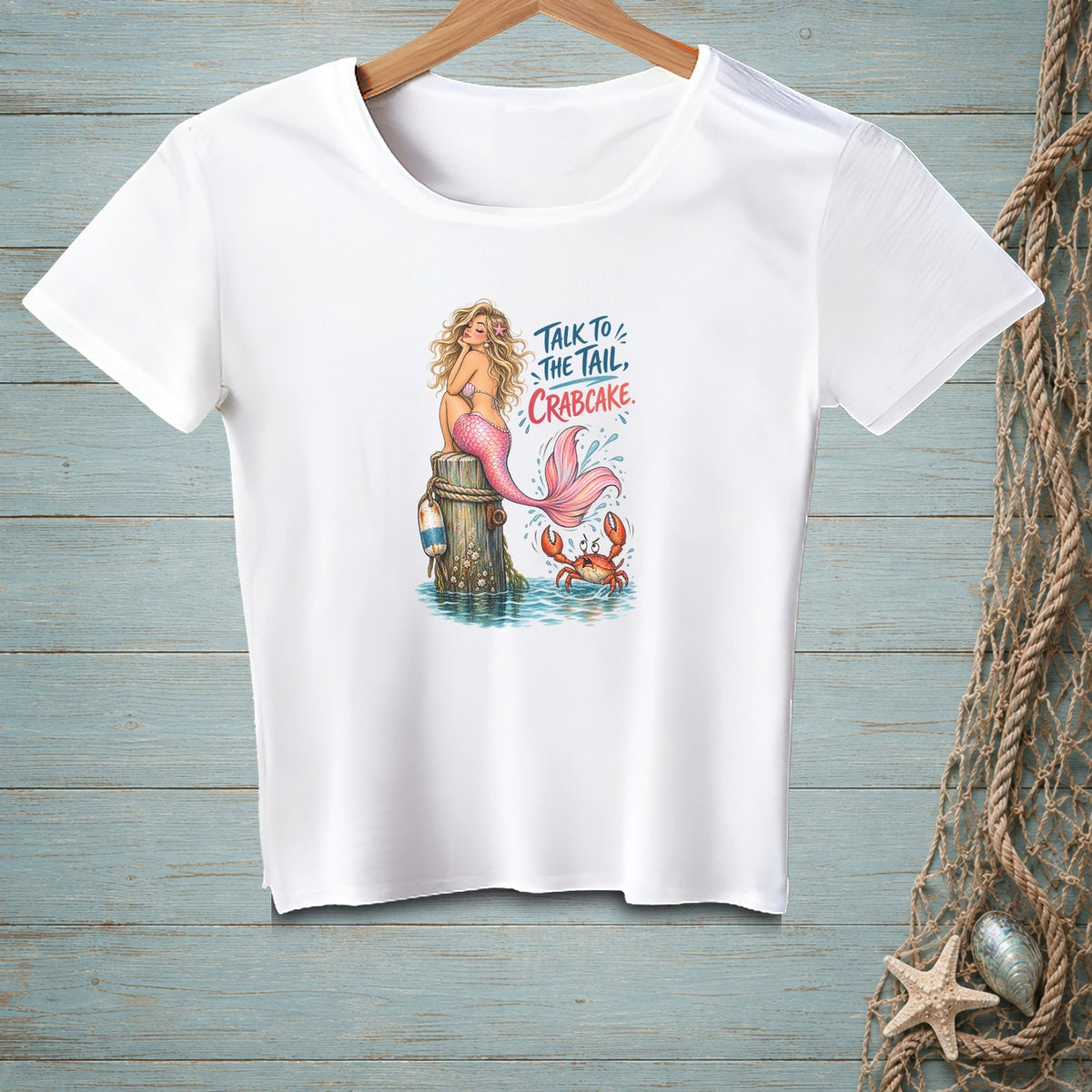 White t-shirt with a graphic of a mermaid and crab and the text "Talk to the tail, crabcake."