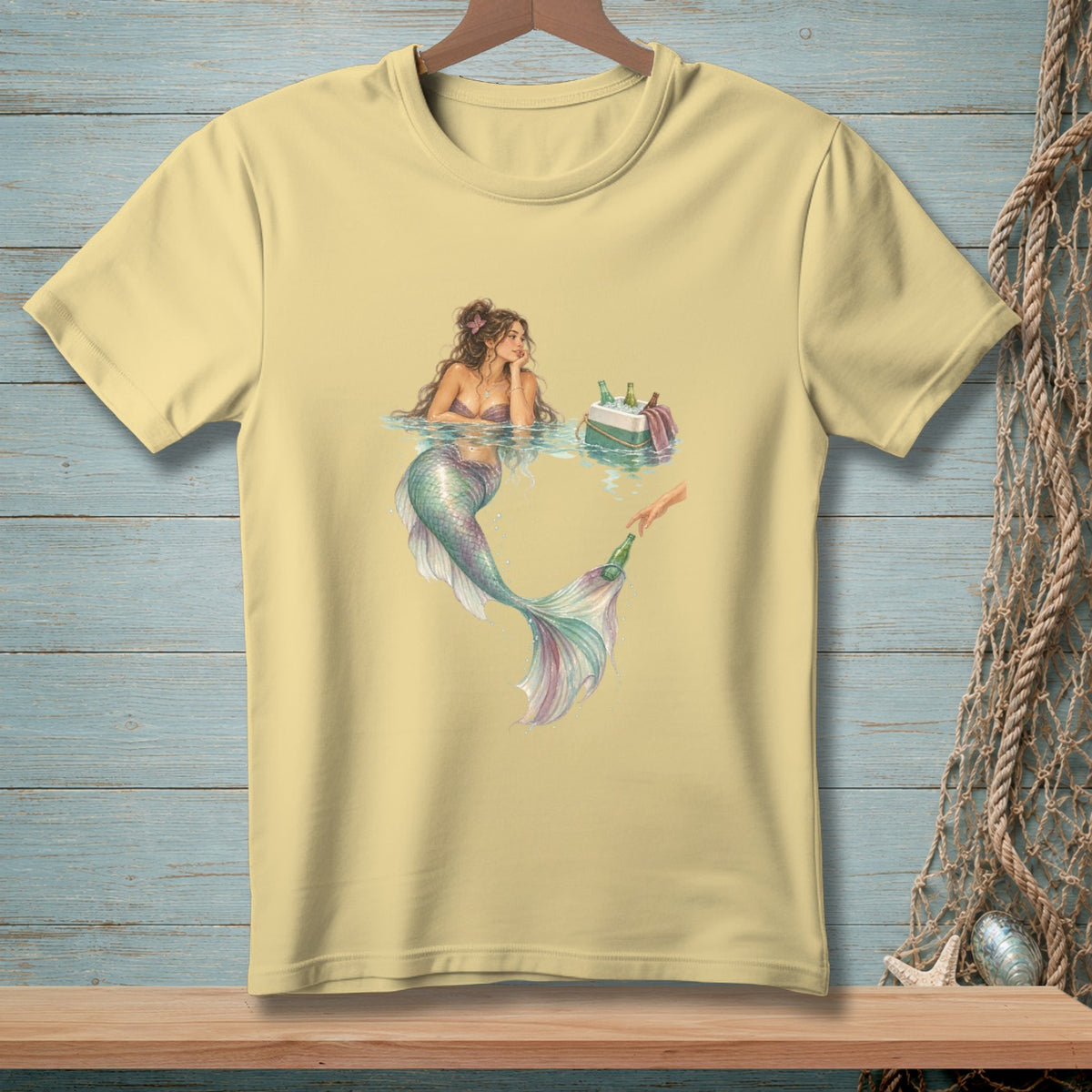 Pale yellow t-shirt with a watercolor illustration of a mermaid and a hand reaching for a bottle.