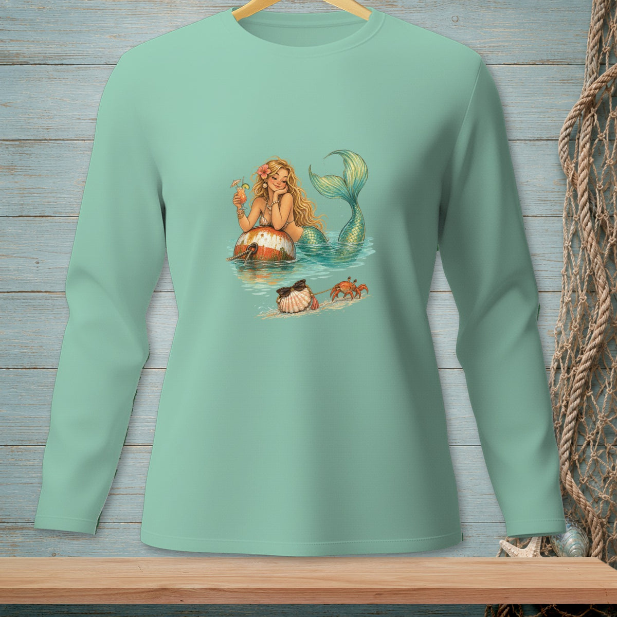 Mermaid relaxing with a drink on a buoy, with a crab and seashell on the sand.