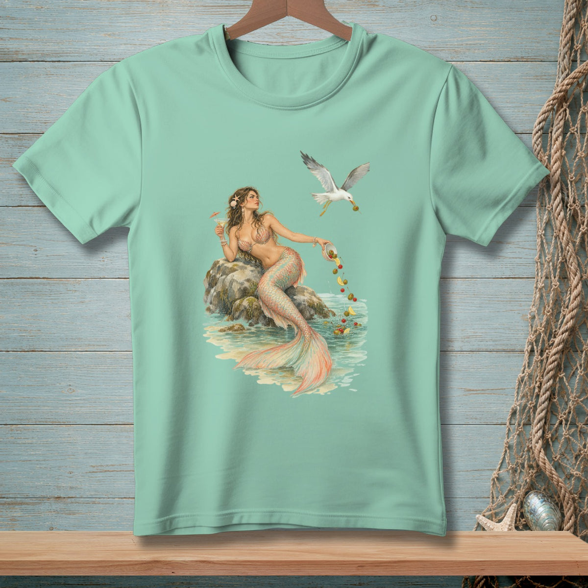 Mint t-shirt with a mermaid sitting on a rock, and a seagull dropping olives into the water.