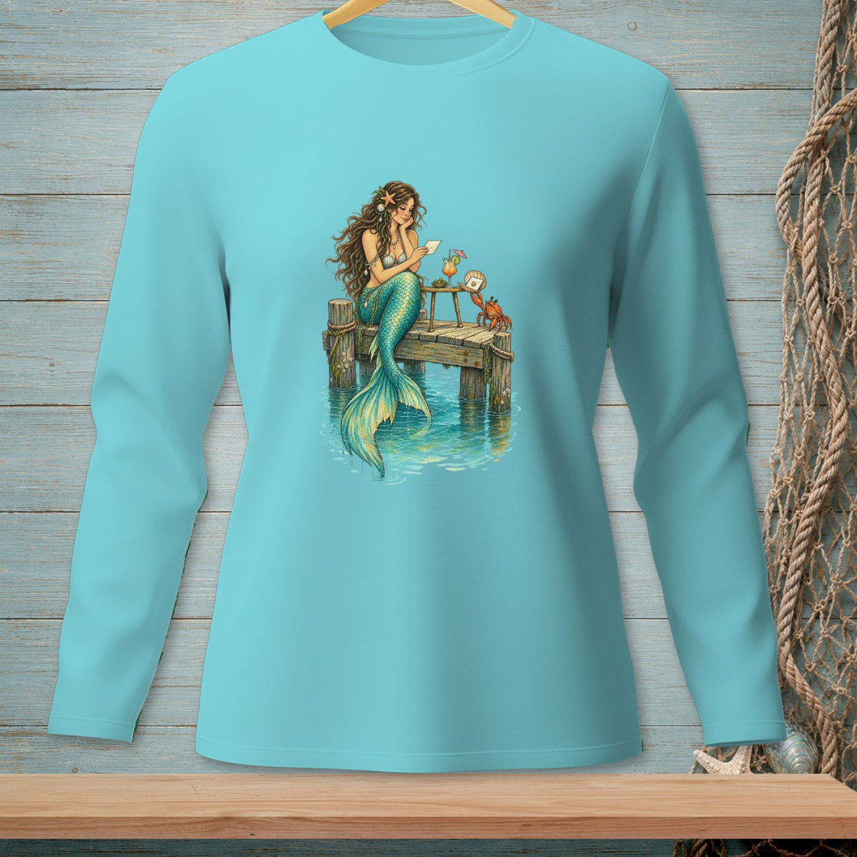 Long sleeve blue shirt with a graphic of a mermaid on a dock.