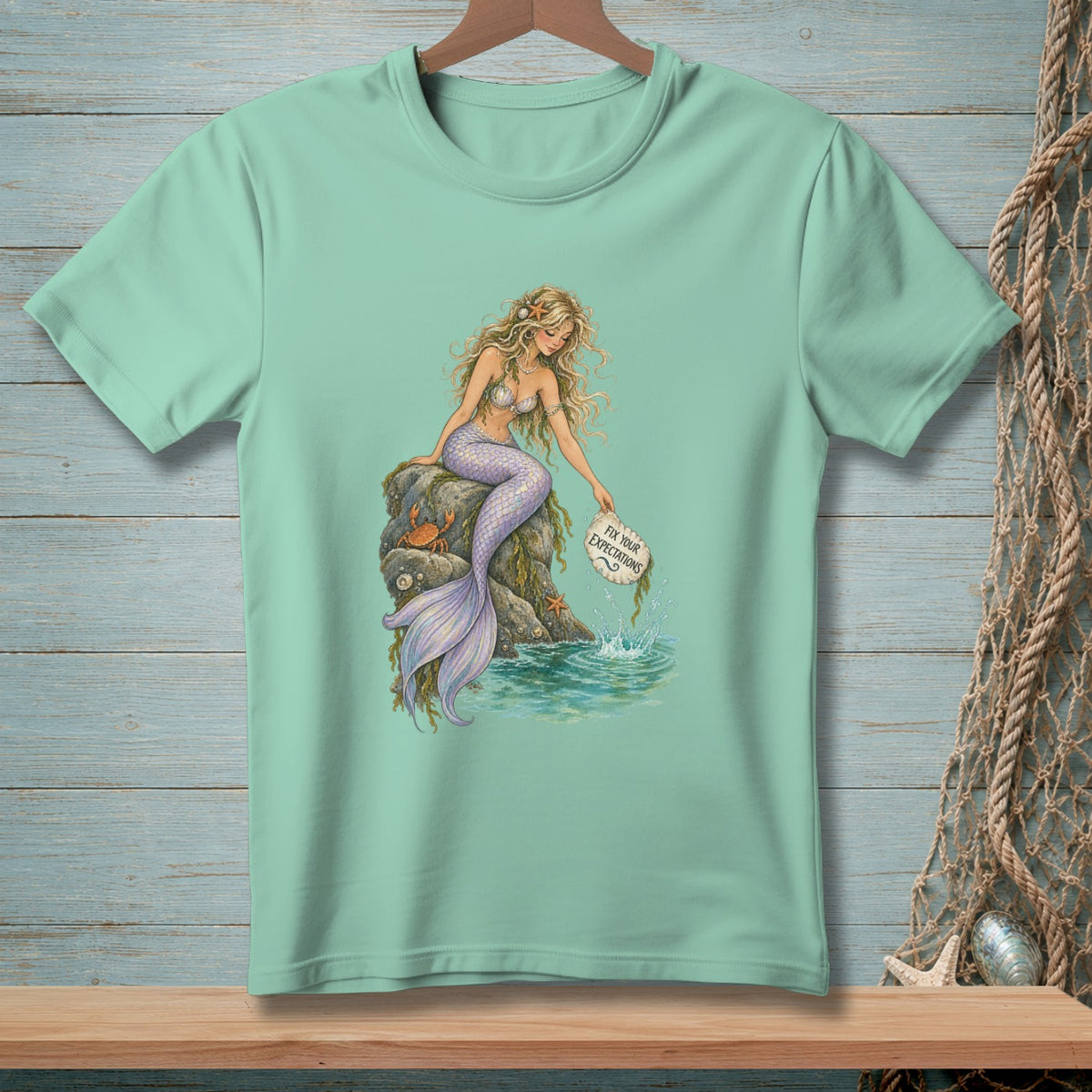 Mermaid on rocks drops a sign reading "Fix Your Expectations" into the water.