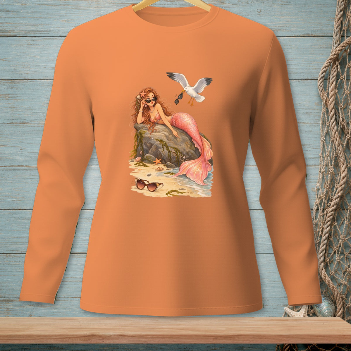 Long-sleeved orange t-shirt with a graphic of a mermaid and seagull at the beach.