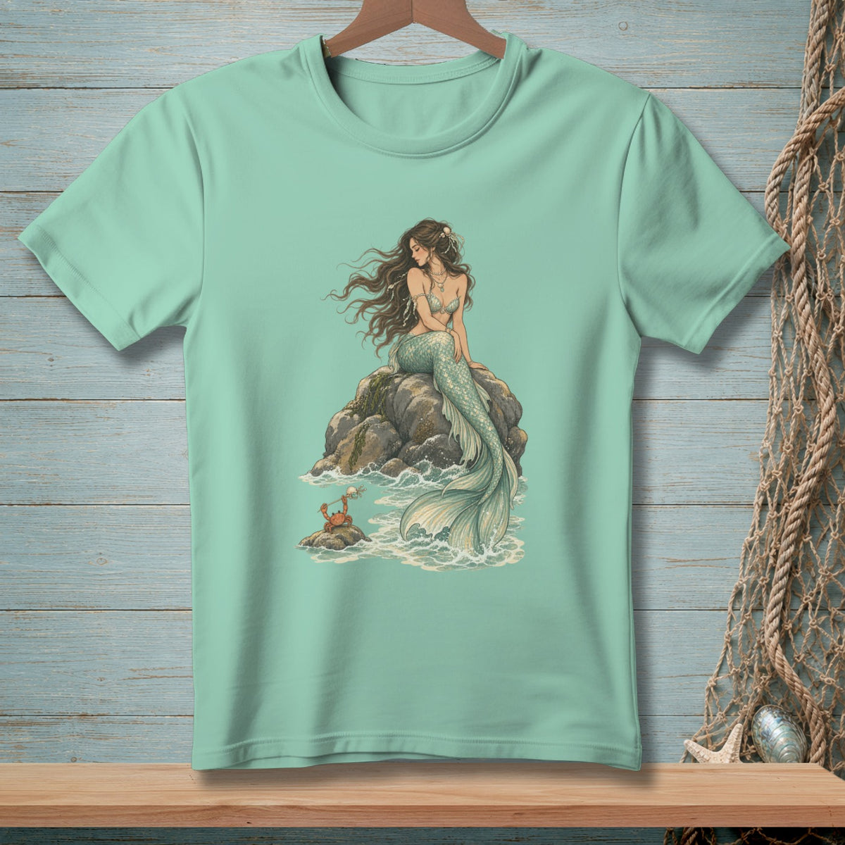Mint green t-shirt with mermaid on a rock and a crab in the waves.
