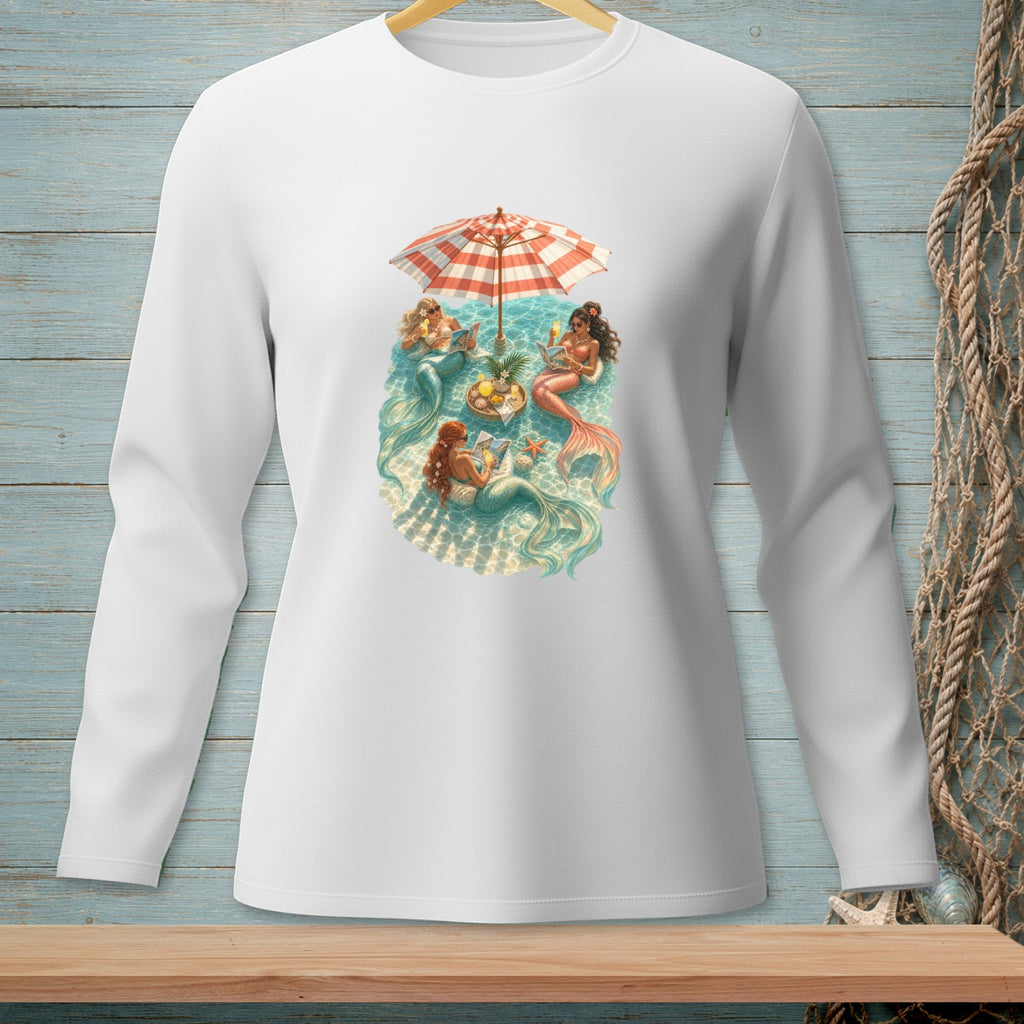 Mermaids relax under a beach umbrella with drinks and snacks in the water.