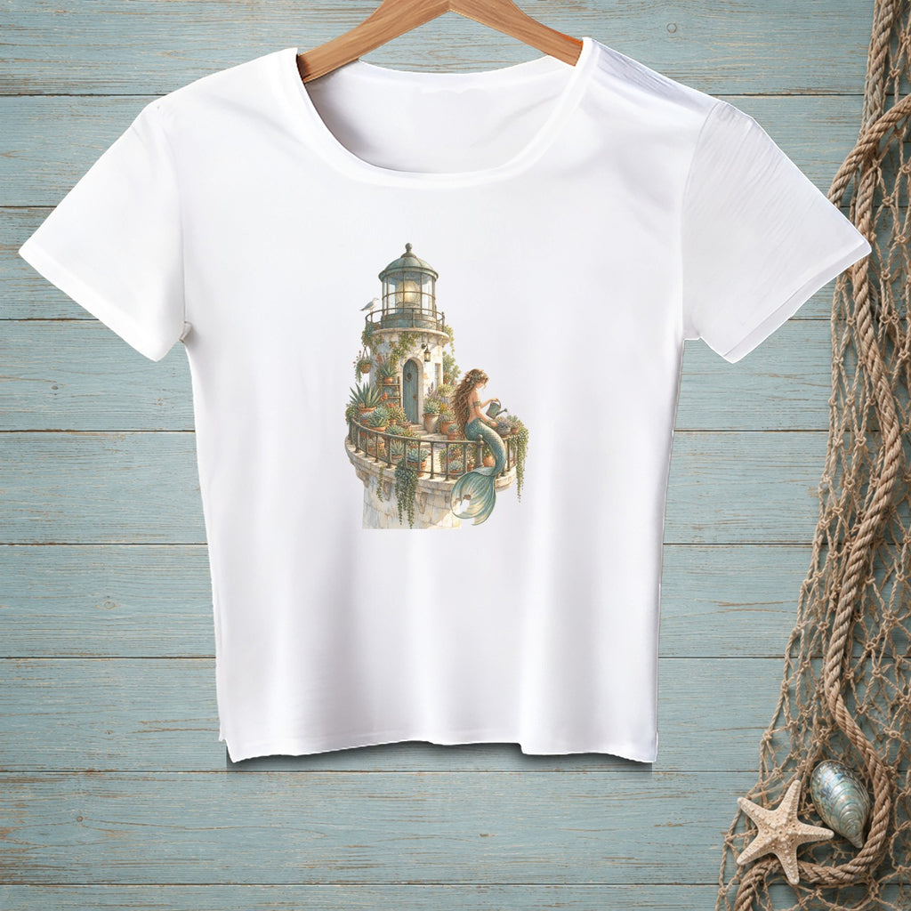 White t-shirt with a watercolor print of a lighthouse and a mermaid on a balcony.