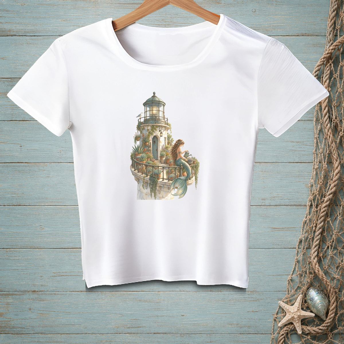 White t-shirt with a watercolor print of a lighthouse and a mermaid on a balcony.