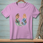 Two mermaids sitting on rocks with waves around them on a pink t-shirt.