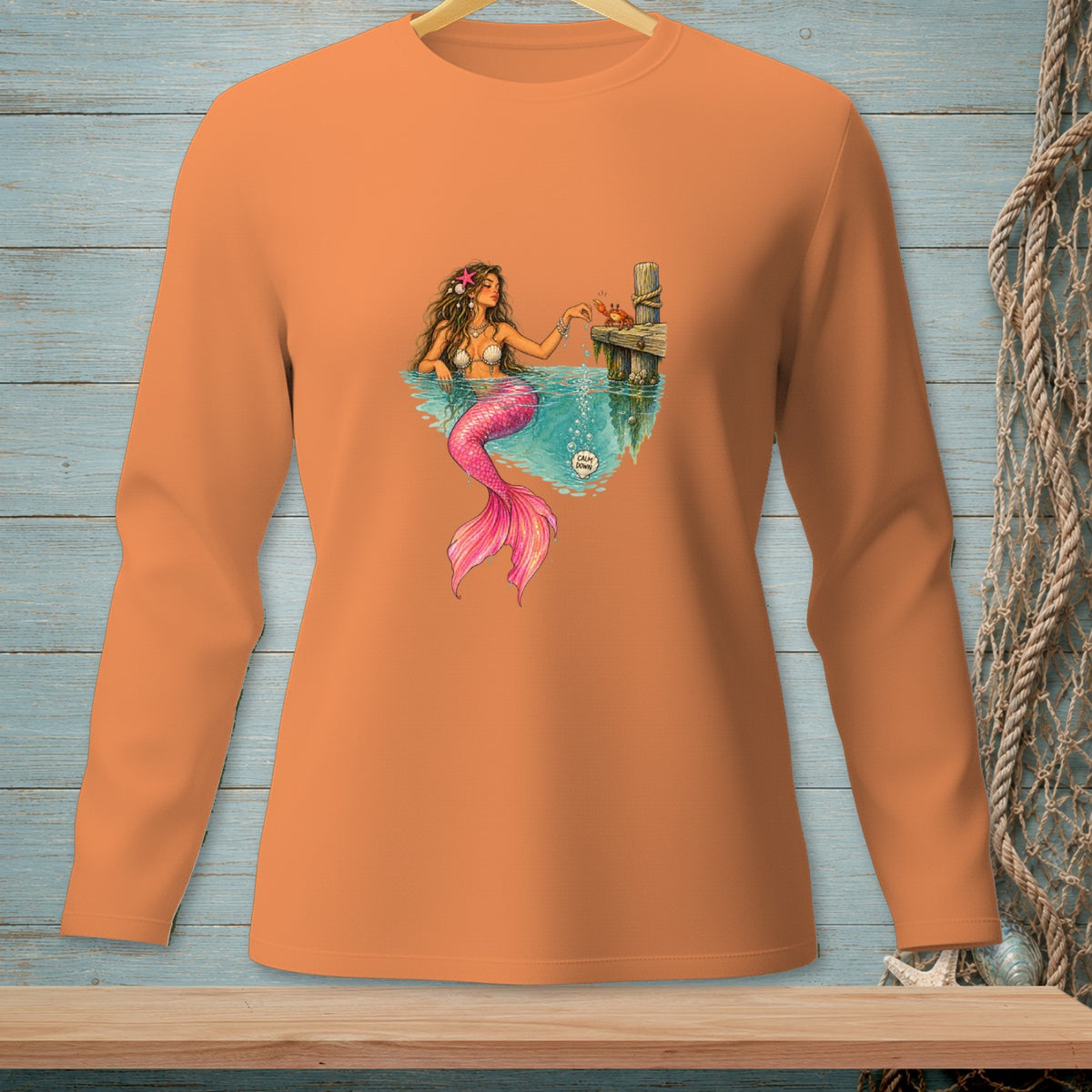 Illustration of a mermaid on an orange long-sleeve shirt with a crab on a dock.