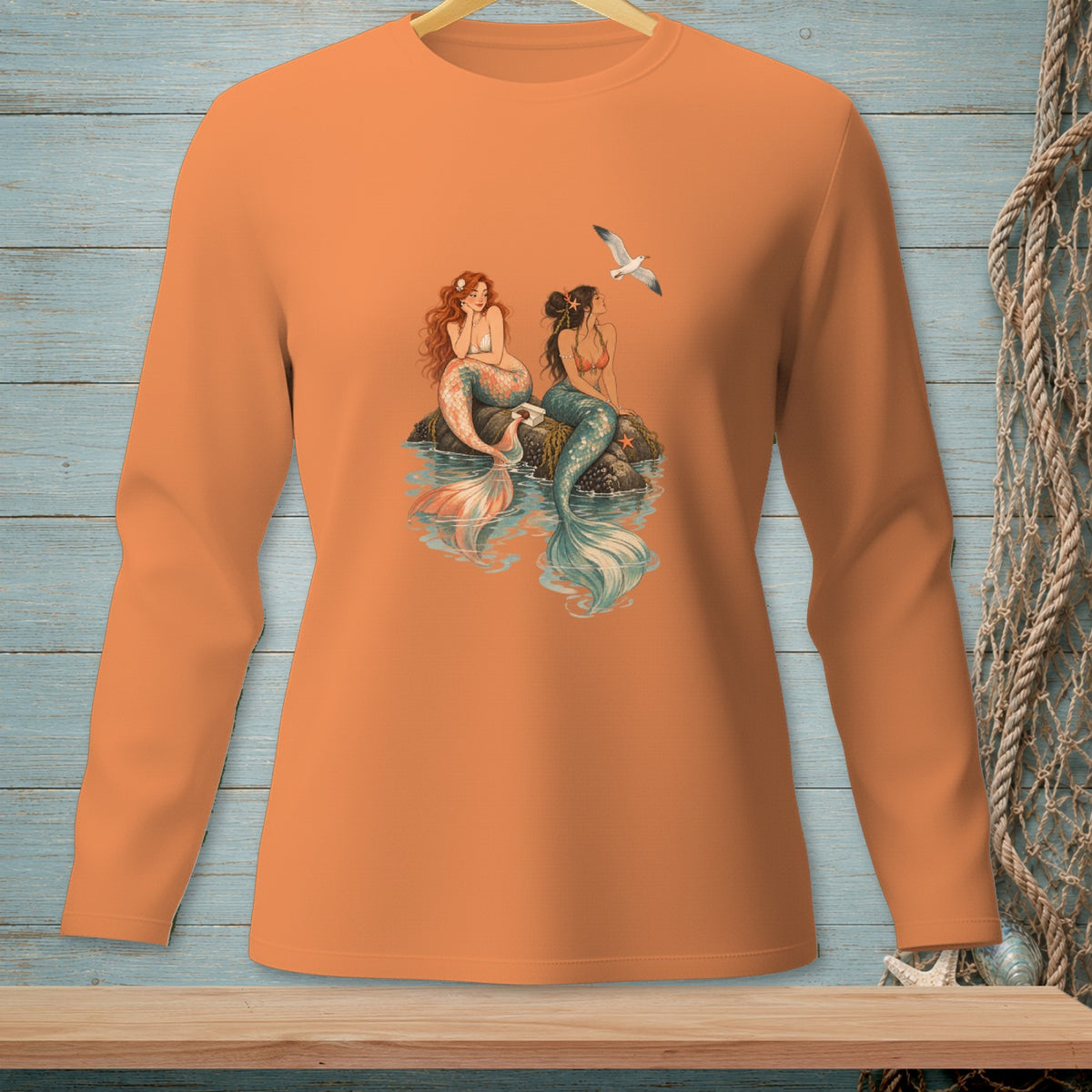 Two mermaids sit on rocks in the water with a seagull flying overhead.