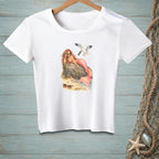 White t-shirt with a mermaid wearing sunglasses relaxing by a rock with a seagull flying above.