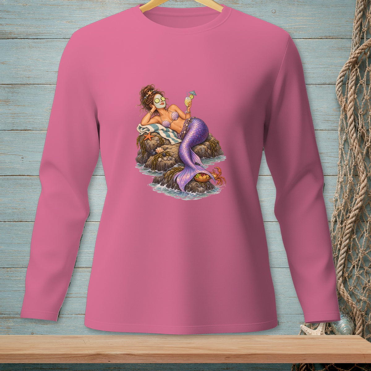 Pink long-sleeve shirt with a mermaid lounging on rocks, holding a drink.
