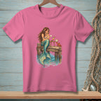 Pink t-shirt with a mermaid sitting on a dock reading a letter with a crab nearby.