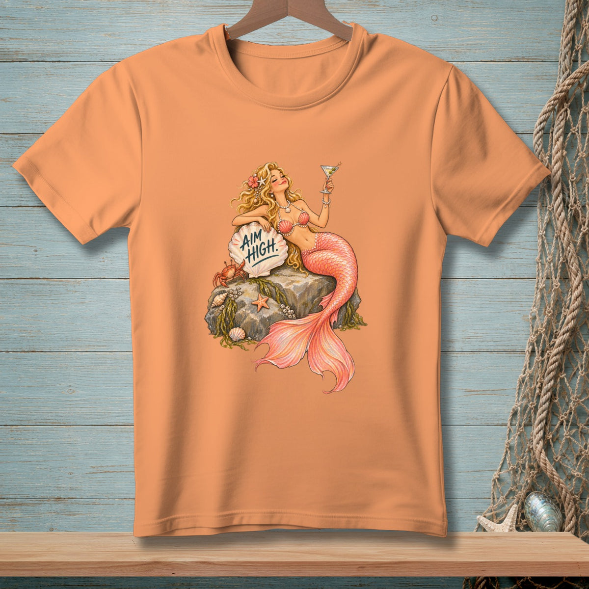 Peach t-shirt with a mermaid holding a martini and text that reads "Aim High."