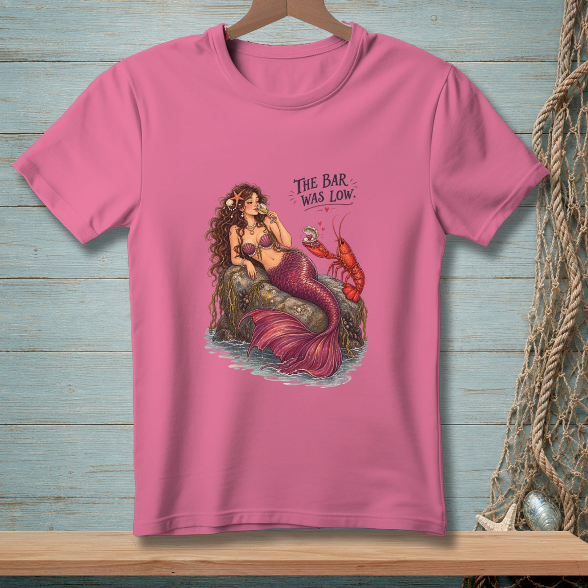 Pink t-shirt with a mermaid, lobster, and text reading "The Bar Was Low."